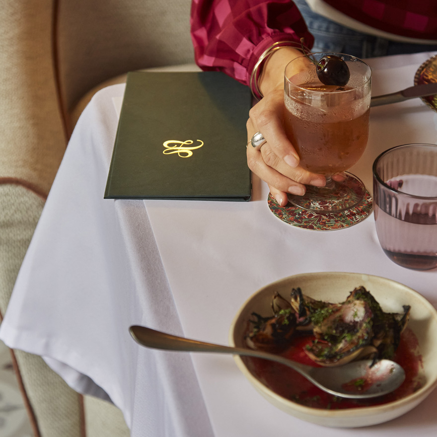 Hand holding a drink, a plates of food and a menu at Leydi restaurant, Hyde London